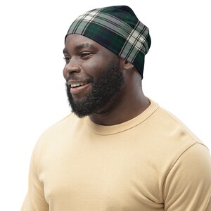 May include: A man wearing a tan sweater and a black, white, and green plaid beanie.