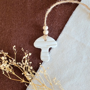 May include: A white ceramic mushroom charm with a textured surface, hanging from a twine string with two wooden beads.