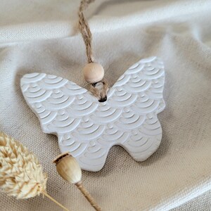 May include: White ceramic butterfly ornament with a textured pattern, hanging from a twine string with a wooden bead.