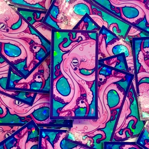 May include: A stack of holographic stickers featuring a pink octopus with iridescent blue and green accents. The octopus is depicted with multiple tentacles and a large eye.
