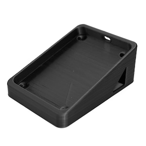 May include: Black plastic wall mount with a rectangular opening. The mount has a slanted base and a small triangular cutout on the side.