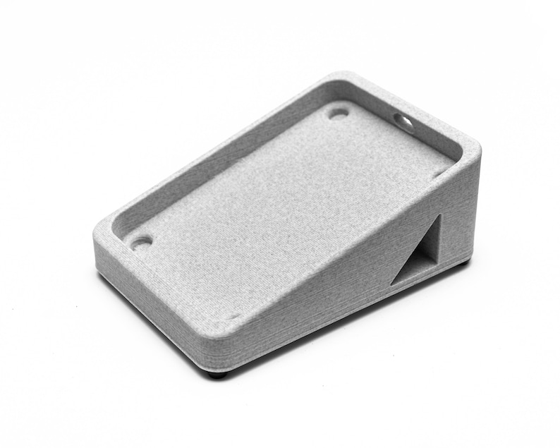 May include: A gray plastic stand with a rectangular base and a sloped top. The stand has two holes on the top and a triangular cutout on the side.
