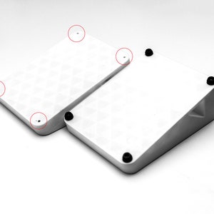 May include: Two white square-shaped platforms with rounded corners. The smaller platform is angled and sits on top of the larger platform. Both platforms have black rubber feet on the bottom.