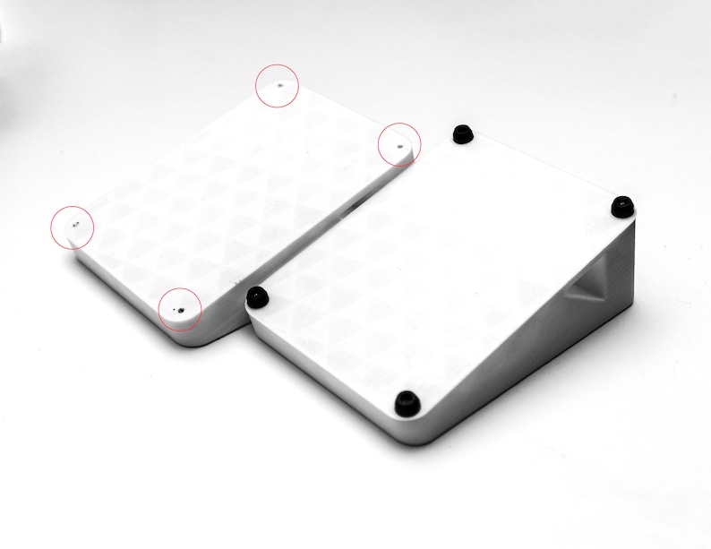 May include: Two white square-shaped platforms with rounded corners. The smaller platform is angled and sits on top of the larger platform. Both platforms have black rubber feet on the bottom.