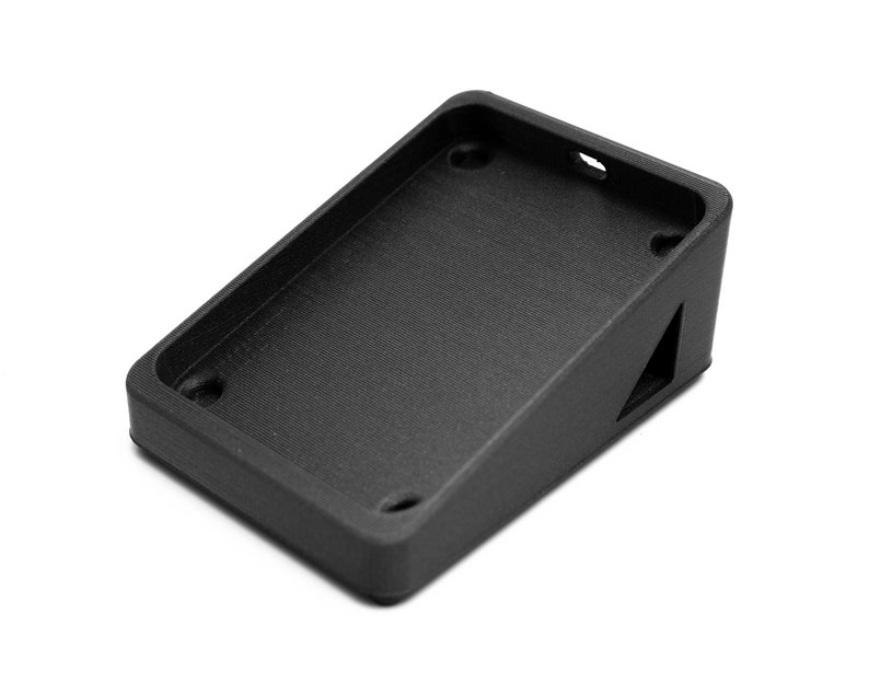 May include: A black plastic phone stand with a raised edge and a triangular cutout on the side.