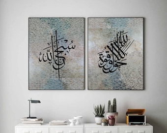 May include: Two framed canvas prints with Arabic calligraphy in black on a textured blue and gray background. The text on the left print reads "Allah" and the text on the right print reads "Subhana Allah Wa Bihamdihi".