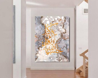 May include: A white canvas with a gold Arabic calligraphy design on a marble background. The text reads "Allah is with those who are patient". The canvas is hanging on a white wall in a hallway with a wooden staircase in the background.