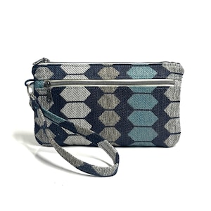 Könnte beinhalten: Rechteckige Clutch mit einem geometrischen Muster in Blau-, Grau- und Türkistönen. Die Clutch hat ein Hauptfach mit Reißverschluss und eine kleinere Reißverschlusstasche auf der Vorderseite. Eine Handschlaufe ist befestigt.