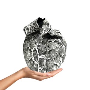 Könnte beinhalten: Eine schwarze und weiße Tasche aus Schlangenleder mit Kordelzug. Die Tasche ist oben zusammengezogen und mit einer schwarzen Kordel gebunden.
