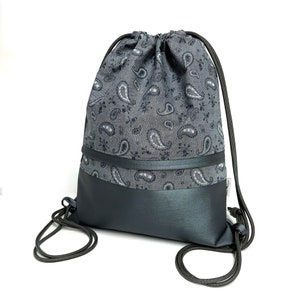 Könnte beinhalten: Eine graue Kordeltasche mit Paisley-Muster und schwarzem Lederboden. Die Tasche hat einen Kordelverschluss und zwei lange Riemen.