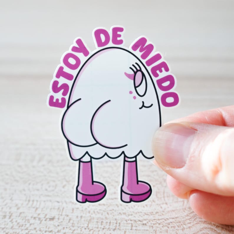 May include: A white sticker featuring a cartoon ghost-like character with pink boots and the Spanish text "ESTOY DE MIEDO" in a pink arch above the character. The character has a surprised expression.