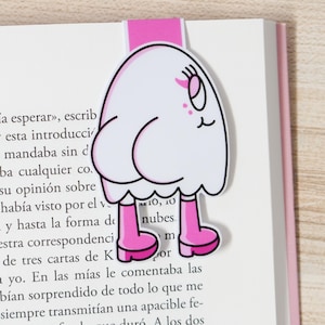 K&ouml;nnte beinhalten: Ein skurriles Lesezeichen mit einem Cartoon-Geist-Design. Der wei&szlig;e Geist hat rosa Stiefel und einen rosa Tab. Das Lesezeichen befindet sich auf den Seiten eines Buches.