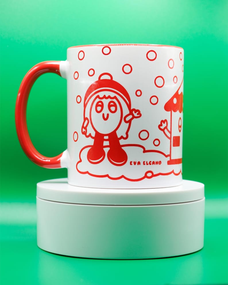 May include: White ceramic mug with a red handle and rim, featuring a whimsical red illustration of a character and a house. The mug has the text "EVA ELCANO" printed on it, and is set against a green background.