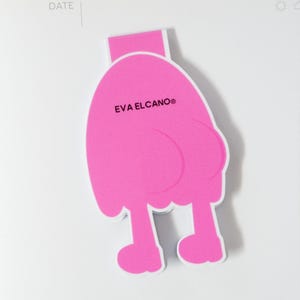 K&ouml;nnte beinhalten: Ein leuchtend pinkfarbener Lesezeichen in Form einer Cartoonfigur mit Beinen und rundem K&ouml;rper. Der Text "EVA ELCANO&reg;" ist auf dem K&ouml;rper aufgedruckt. Das Lesezeichen befindet sich auf wei&szlig;em Hintergrund.