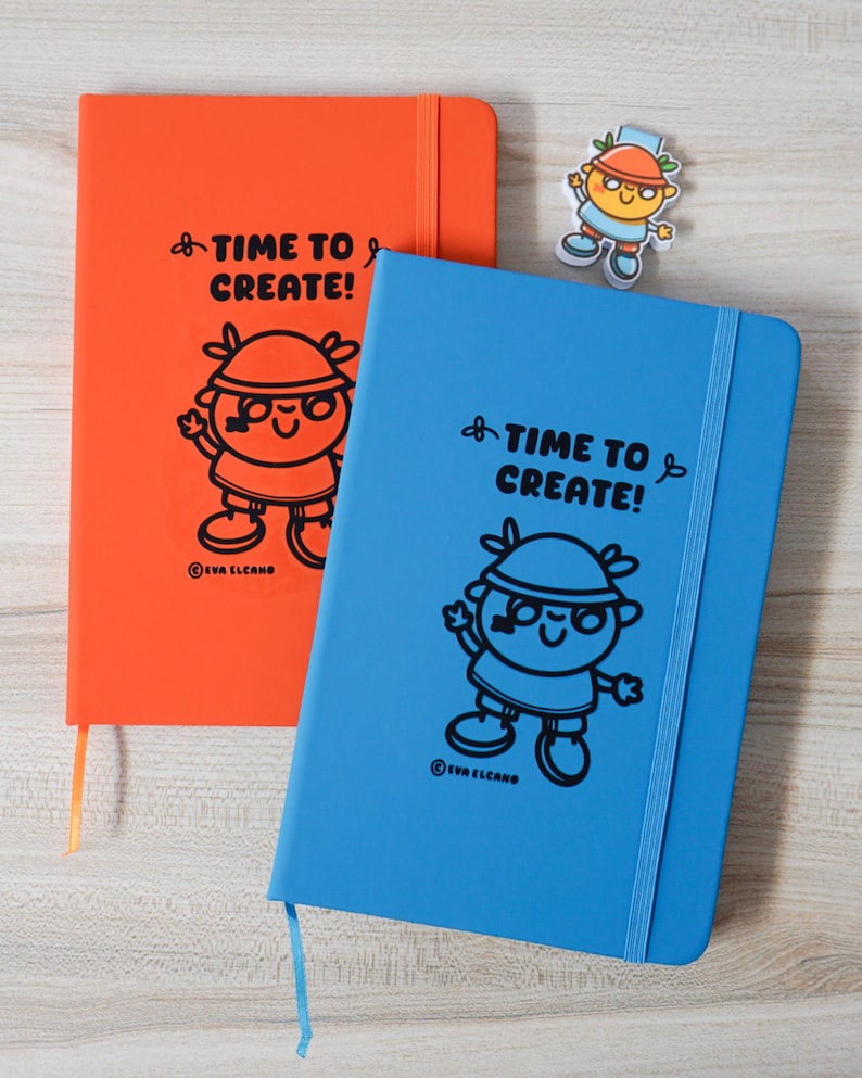 May include: Two notebooks, one orange and one blue, featuring the text "TIME TO CREATE!" and a cartoon character illustration. A small sticker of the same character is also present. The notebooks have a ribbon bookmark and the brand name "EVA ELCANO" is printed.