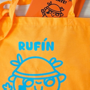 Może przedstawiać: Pomarańczowa torba z napisem "RUFIN" w niebieskich literach i projektem postaci z kresk&oacute;wki. Wewnątrz pomarańczowy notatnik z napisem "TIME TO CREATE!" i pasującą postacią z kresk&oacute;wki.