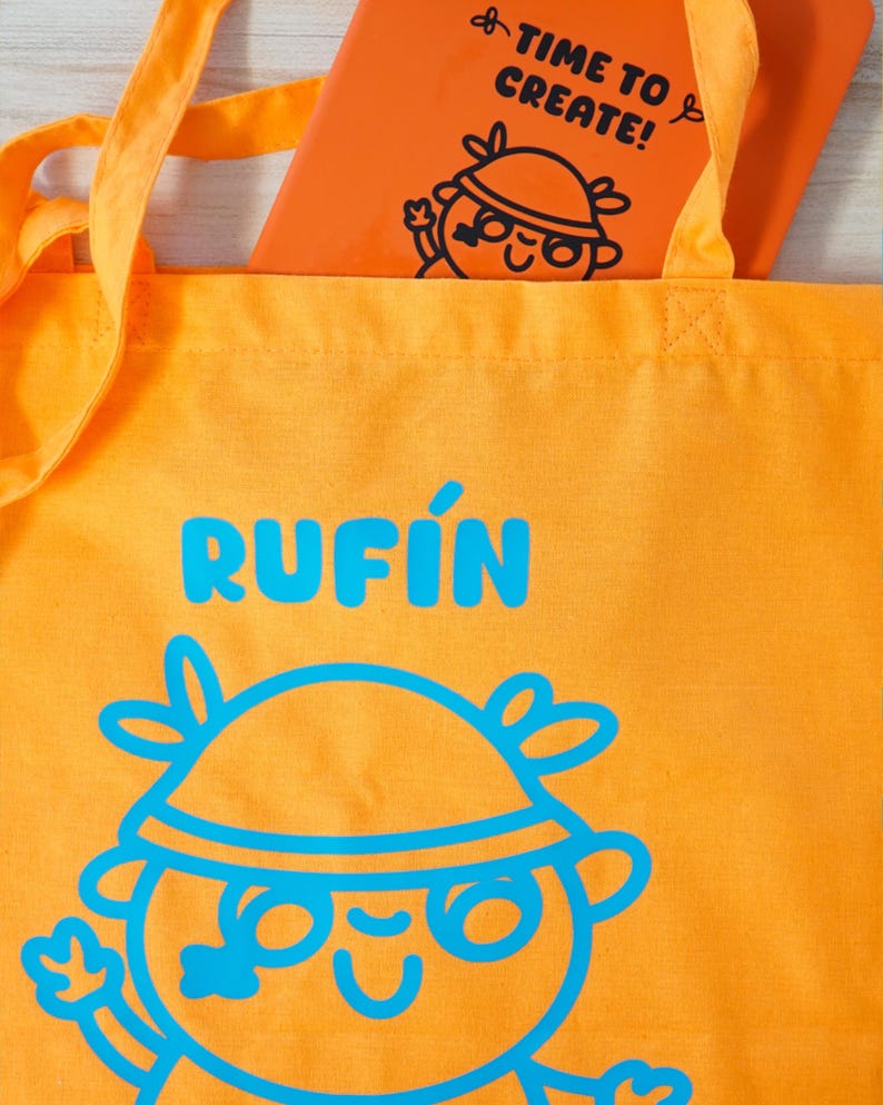 Może przedstawiać: Pomarańczowa torba z napisem "RUFIN" w niebieskich literach i projektem postaci z kresk&oacute;wki. Wewnątrz pomarańczowy notatnik z napisem "TIME TO CREATE!" i pasującą postacią z kresk&oacute;wki.