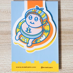 May include: A whimsical sticker featuring a cartoon character in a yellow and blue striped hat and inner tube. The character is surrounded by a yellow and orange floral design, set against a light blue background. The sticker has the website address www.evaelcano.com and the Instagram handle @evaelcano.