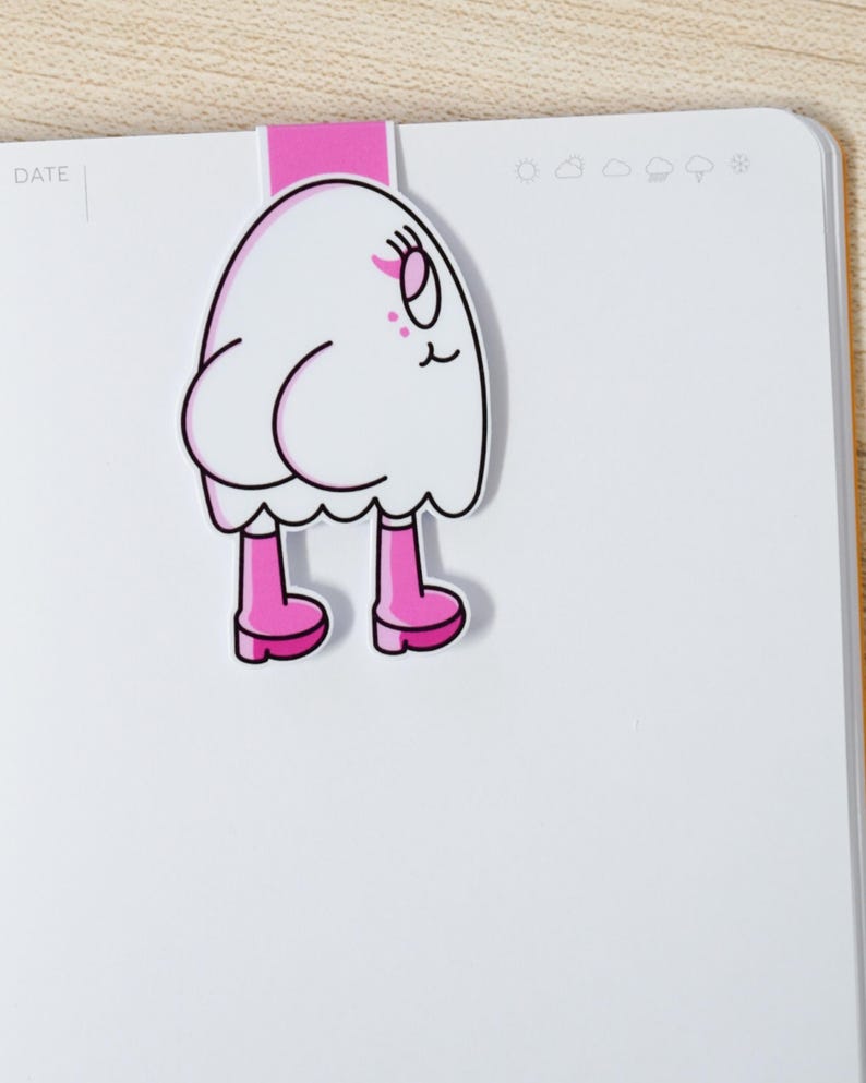 K&ouml;nnte beinhalten: Ein wei&szlig;er, cartoonartiger Lesezeichen in Geisterform mit rosa Stiefeln und einem rosa Oberteil. Das Lesezeichen ist an einem wei&szlig;en Notizbuch befestigt. Der Geist hat ein l&auml;chelndes Gesicht mit rosa Akzenten. Das Notizbuch hat das Wort "DATE" links oben aufgedruckt.