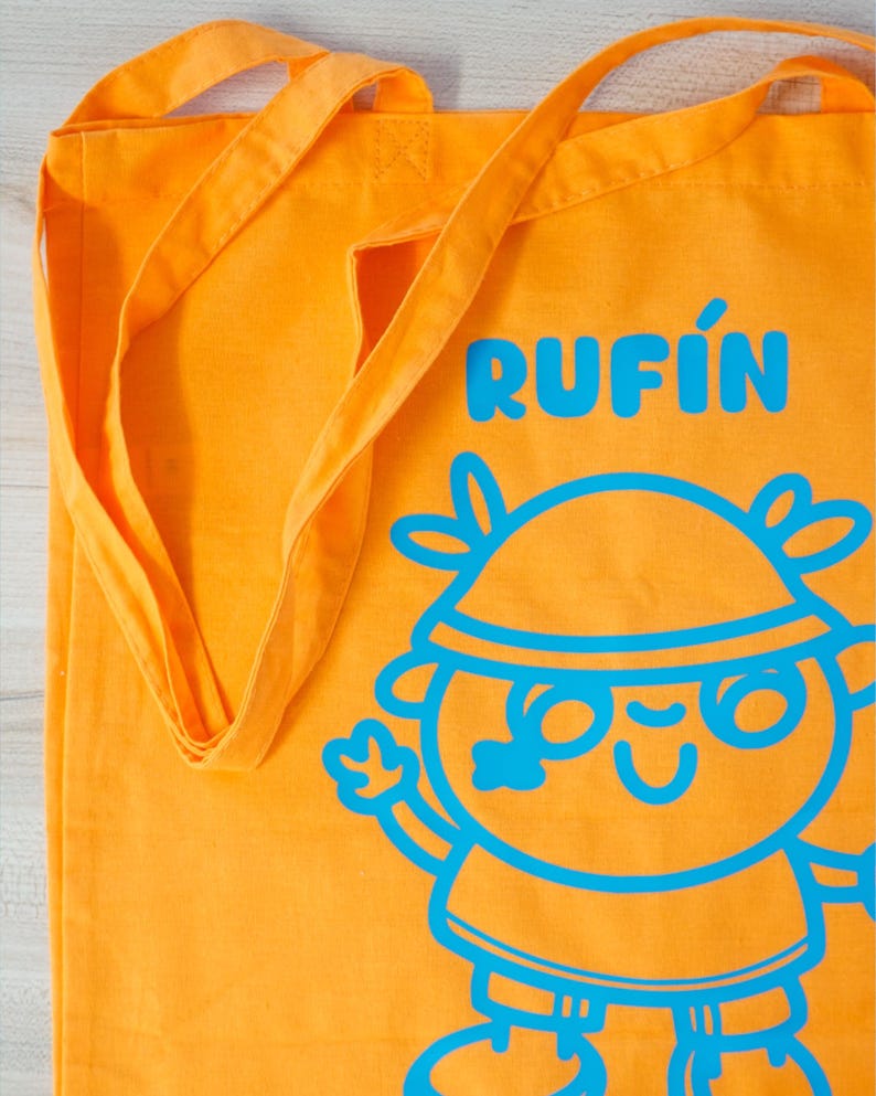 Może przedstawiać: Pomarańczowa torba typu tote z długimi paskami. Torba zawiera słowo "RUFIN" w kolorze niebieskim, wraz z ilustracją postaci z kresk&oacute;wki w kolorze niebieskim. Torba jest wykonana z wytrzymałej tkaniny.