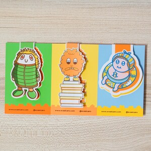 May include: A colorful, three-panel card featuring cartoon characters. The first panel has a green background with a character in a green jacket. The second panel has an orange character on a stack of books. The third panel has a blue background with a character in a hat. The website address and social media handle are at the bottom of each panel.