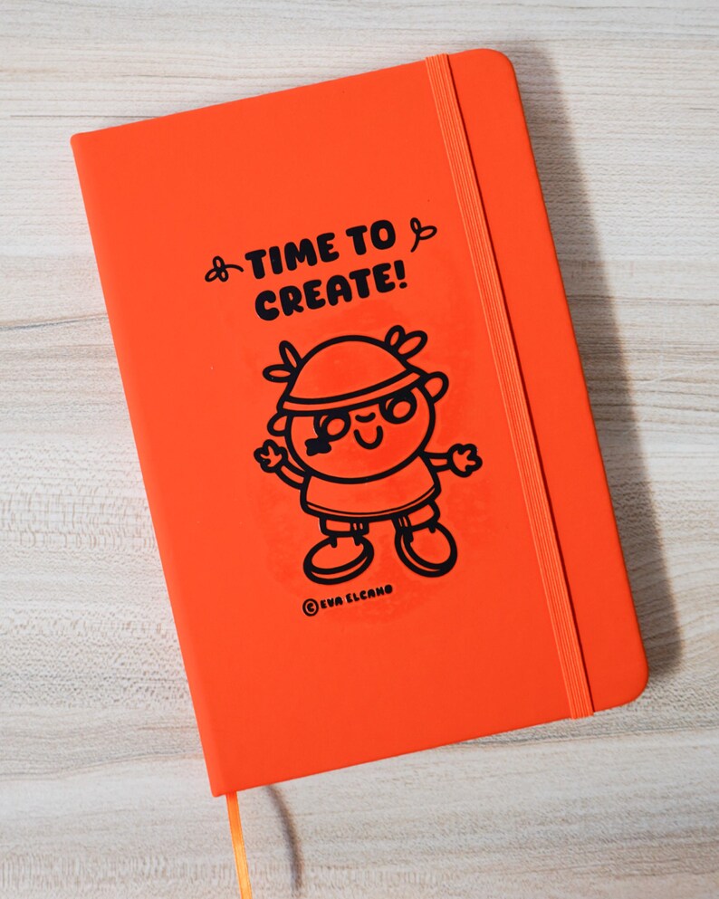 May include: An orange notebook featuring the text "TIME TO CREATE!" and a cartoon character illustration. The notebook has an elastic band closure and a ribbon bookmark. The artist's name, EVA ELCANO, is printed at the bottom.