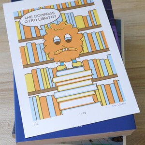 May include: A colorful illustration featuring a cartoon character standing on a stack of books, with a bookshelf background. The character has an orange, fluffy appearance and a speech bubble that says, "&iquest;ME COMPRAS OTRO LIBRITO?" The print is on top of a stack of books.