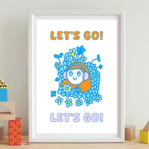 May include: A framed art print featuring a cartoon illustration. The artwork depicts a smiling character with orange hair and pink headphones, surrounded by blue flowers. The words "LET'S GO!" are written in orange and pink.