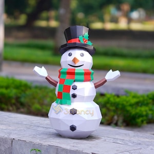 May include: A white, geometric snowman with a black top hat, a red and green scarf, and a carrot nose. The snowman has outstretched arms and black button eyes. The base of the snowman has the text "3Dfancy".