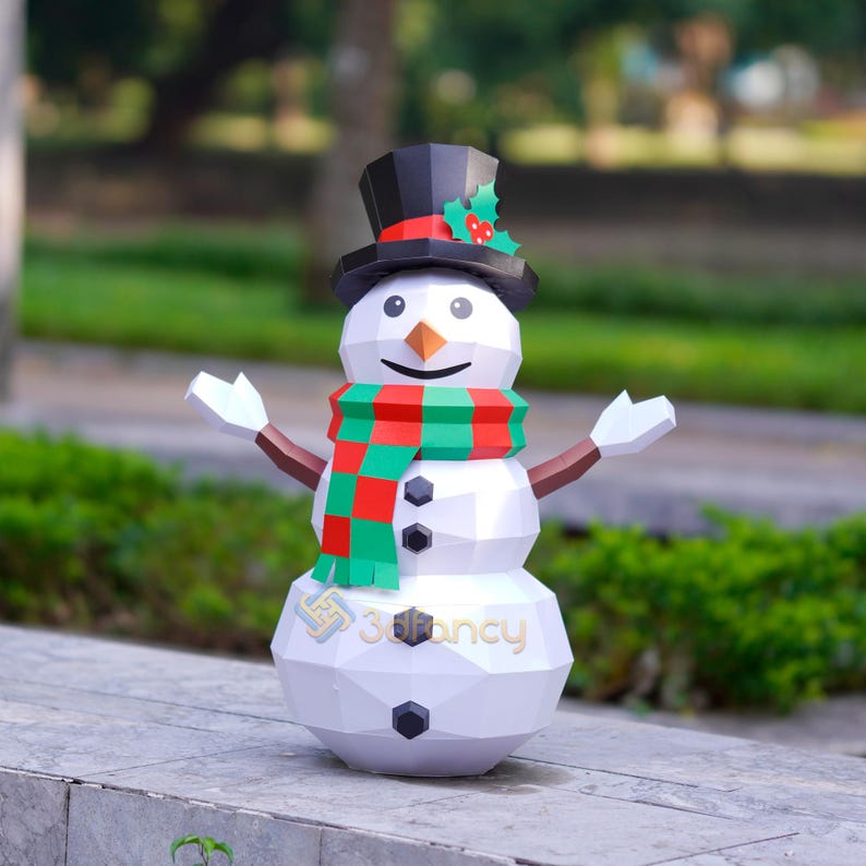May include: A white, geometric snowman with a black top hat, a red and green scarf, and a carrot nose. The snowman has outstretched arms and black button eyes. The base of the snowman has the text "3Dfancy".