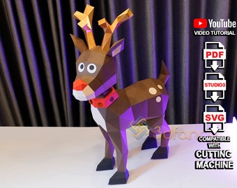 Puede incluir: Un reno de papel marrón con la nariz roja y un collar rojo. El reno está de pie sobre una superficie blanca. La imagen incluye texto que dice "YouTube Video Tutorial", "PDF", "STUDIO3", "SVG", "Compatible with Cutting Machine".