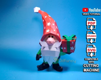 May include: A papercraft Christmas gnome with a red hat adorned with white stars, holding a gift box. The gnome has a white beard, green body, and black shoes. The image includes text: "YouTube Video Tutorial", "PDF", "Studio3", "SVG", and "Compatible with Cutting Machine."