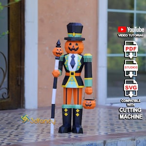 Könnte beinhalten: Eine geometrische Nussknacker-Figur aus Papier mit Kürbiskopf, die einen schwarzen Zylinder und eine schwarz-türkise Uniform mit gelben Akzenten trägt, einen Stab mit kleinem Kürbis hält und einen passenden kürbisförmigen Eimer trägt.