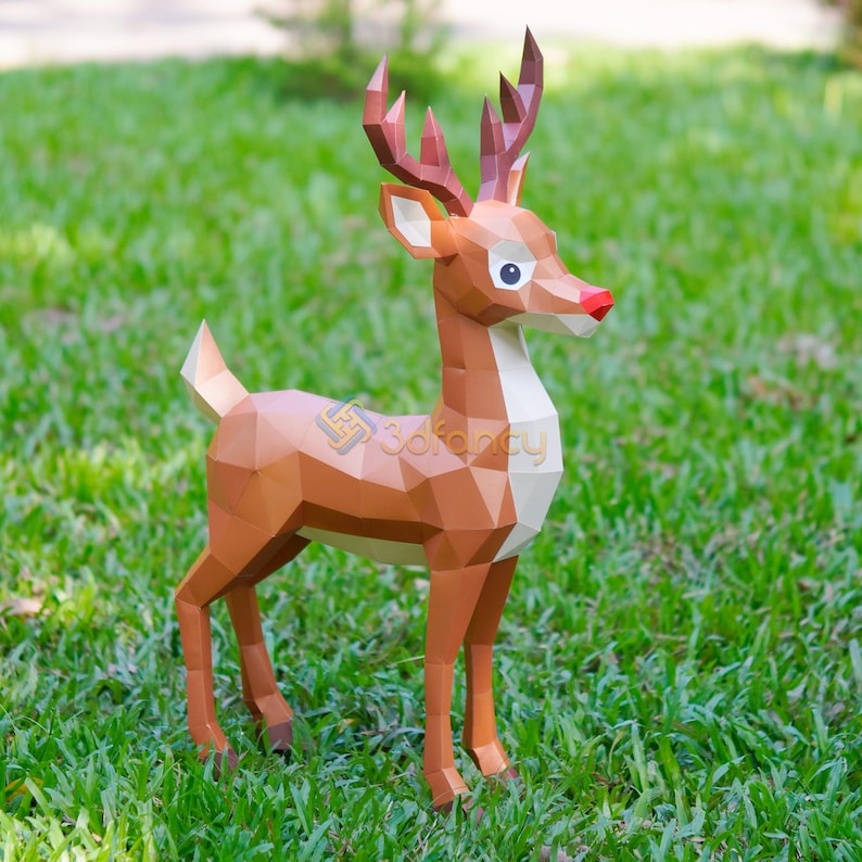 May include: A brown papercraft deer with a red nose, white chest, and large antlers stands on green grass. The geometric design gives the deer a modern, polygonal look. The deer is a festive decoration.