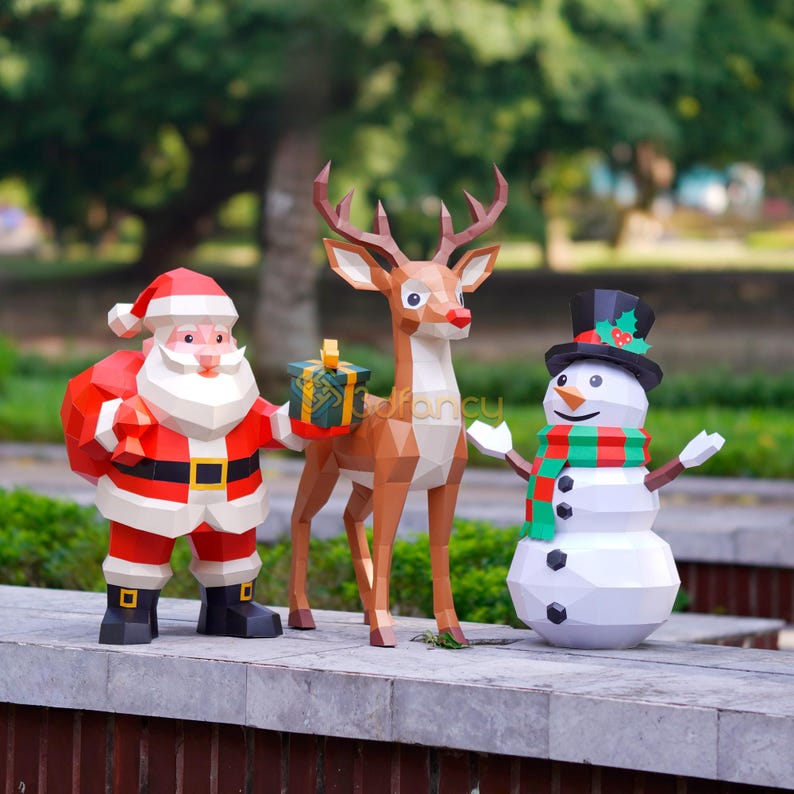May include: A festive Christmas display featuring papercraft figures of Santa Claus, a reindeer, and a snowman. Santa wears a red suit and carries a sack. The reindeer holds a gift box. The snowman has a top hat and scarf.