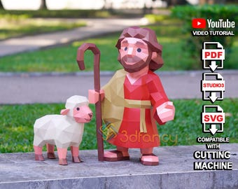 May include: A papercraft shepherd figure in red and tan robes, holding a staff, stands next to a white and pink lamb. The image includes text for a YouTube video tutorial and file formats: PDF, STUDIO3, and SVG, compatible with a cutting machine.