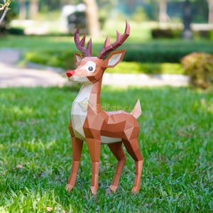 May include: A brown papercraft reindeer with a red nose, white chest, and brown antlers stands on green grass. The geometric design gives the reindeer a modern look. The reindeer is a festive decoration.
