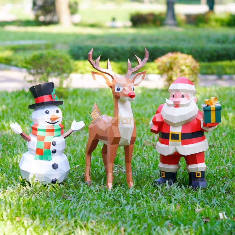 May include: A festive outdoor scene featuring three geometric paper Christmas decorations. A snowman with a top hat and scarf, a reindeer, and Santa Claus holding a gift box stand on green grass.