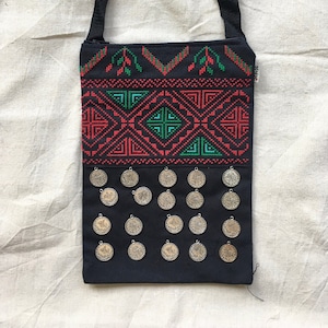 Puede incluir: Bolso bandolera negro con un patrón geométrico rojo y verde y detalles de monedas plateadas.