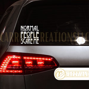 May include: A white vinyl decal with the text "NORMAL PEOPLE SCARE ME" on a black car window. The decal is on the back window of a silver car. The car has red taillights. The decal is from Carrillo Creations.