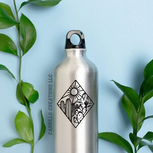 May include: A silver water bottle with a black lid and a black and white graphic of a desert scene with a sun, cacti, and mountains. The graphic is in a diamond shape. The text "CARRILLO CREATIONS LLC" is printed on the side of the bottle.