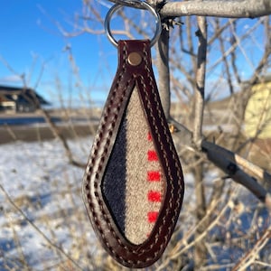 May include: A brown leather keychain with a diamond-shaped window that reveals a patterned fabric with red, white, and blue colors.