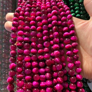 May include: A strand of pink tiger's eye beads. The beads are round and have a shiny, iridescent finish.