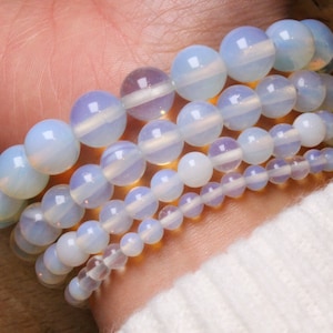 Peut inclure: Un ensemble de quatre bracelets en opale blanche. Les bracelets sont empilés sur le poignet d'une personne.