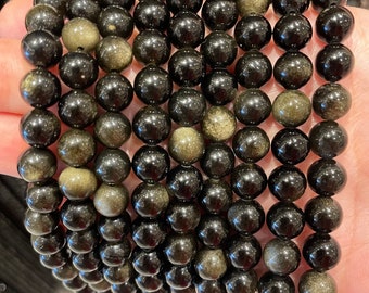 May include: A strand of black obsidian beads with gold flecks. The beads are round and smooth, and they are strung on a clear elastic cord.
