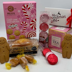 May include: A holiday gift set featuring a pink box of Reids Scottish Candy Cane Shortbreads, a white Merry Christmas box with a red ribbon, a box of Afternoon Tea, a cherry and almond cake, three gingerbread men, and assorted wrapped candies.