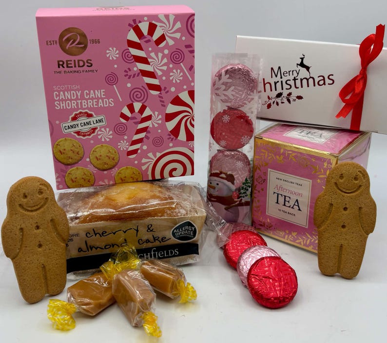 May include: A holiday gift set featuring a pink box of Reids Scottish Candy Cane Shortbreads, a white Merry Christmas box with a red ribbon, a box of Afternoon Tea, a cherry and almond cake, three gingerbread men, and assorted wrapped candies.