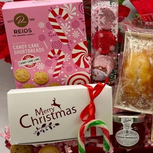 May include: A holiday gift set featuring a pink box of Reids Scottish Candy Cane Shortbreads, a clear tube of three foil-wrapped chocolates, a white box labeled Merry Christmas with a red ribbon and candy cane, and a jar of orange marmalade.