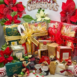 May include: A Christmas gift basket containing various tea boxes, shortbread, Christmas pudding, jam jars, and a gingerbread man cookie. The items are wrapped in clear cellophane with gold and red ribbons, decorated with red and white poinsettias.