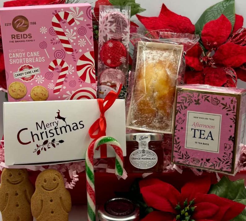 May include: A holiday gift basket containing a pink box of Reids Scottish Candy Cane Shortbreads, a white box labeled Merry Christmas, a package of red foil-wrapped chocolates, a small loaf cake, orange marmalade, and Afternoon Tea.